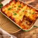 Klassische Lasagne mit Hackfleisch und Béchamelsoße, goldbraun überbacken in einer grünen Auflaufform.